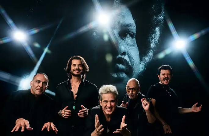 O grupo mineiro Jota Quest oficializou o lançamento do álbum "Jota Quest & Tim Maia - Dance Enquanto é Tempo", projeto dedicado a celebrar o repertório e a sonoridade de um dos maiores ícones da música brasileira. O trabalho chega às plataformas digitais com 16 faixas e ganha também uma versão física em vinil duplo.
Lançado pela Universal Music, o projeto conta com o apoio direto e a aprovação de Carmelo Maia, filho de Tim e gestor do espólio do artista. Além de liberar o uso das gravações originais, Carmelo acompanhou a produção no estúdio e participou ativamente da escolha do repertório.
"O Carmelo não só liberou tudo, mas esteve junto, sugeriu música e co-produziu a coisa toda com a gente. Fica o nosso agradecimento por ele curtir e conviver com a gente nesse processo", destaca o vocalista Rogério Flausino.
Saiba quem são os artistas convidados do novo disco do Jota Quest
Para criar releituras que conectassem o legado de Tim Maia à cena atual, o grupo convidou nomes de destaque do samba, do rap e da nova geração da MPB.
O baixista e produtor PJ reforça que a intenção sempre foi respeitar a essência do "Síndico":
"O Jota Quest faz parte do pop rock, mas traz essa 'black', como o Barão traz o blues e o Skank traz o reggae. Não tivemos receio nenhum, era só a vontade de manter a identidade das músicas do Tim Maia."
Entre as colaborações do álbum estão:
Negra Li: grava o single "Descobridor dos Sete Mares", contribuindo com um trecho em rap inédito. "Ela escreveu algo incrível para homenagear o Tim, foi a cereja do bolo", revela Flausino.
Thiaguinho: divide os vocais em "Réu Confesso", que ganha uma transição para o samba-soul na parte final.
Os Garotin e Carlinhos Brown: somam percussão e vocais na releitura de "Imunização Racional (Que Beleza)".
Tony Tornado & Lincoln Tornado: marcam presença no clássico "Sossego".
Mãeana: traz um toque de bossa nova para "Você / I Don't Know What To Do With Myself".
O que a banda prepara para a estreia do novo show no Rock in Rio
O lançamento do álbum serve como ponto de partida para a nova fase da banda nos palcos. A estreia oficial da turnê acontece no festival Rock in Rio, com um roteiro focado no repertório do homenageado e em resgates do primeiro disco do Jota Quest.
A apresentação conta com um projeto visual exclusivo assinado por Batman Zavareze, adaptado para os painéis de LED do evento.
"É um show completamente novo: parte sonora, visual, tudo. O conteúdo do telão é o principal elemento cênico hoje", afirma Flausino, adiantando que o grupo prepara duas participações especiais mantidas em segredo para a noite do festival.